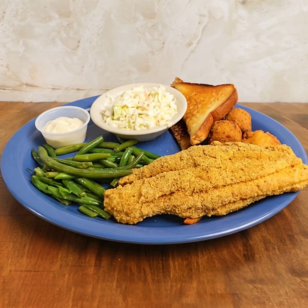 Blue plate of breaded fried fish with green beans, coleslaw, hush puppies, toast, and dipping sauce on a wooden table.