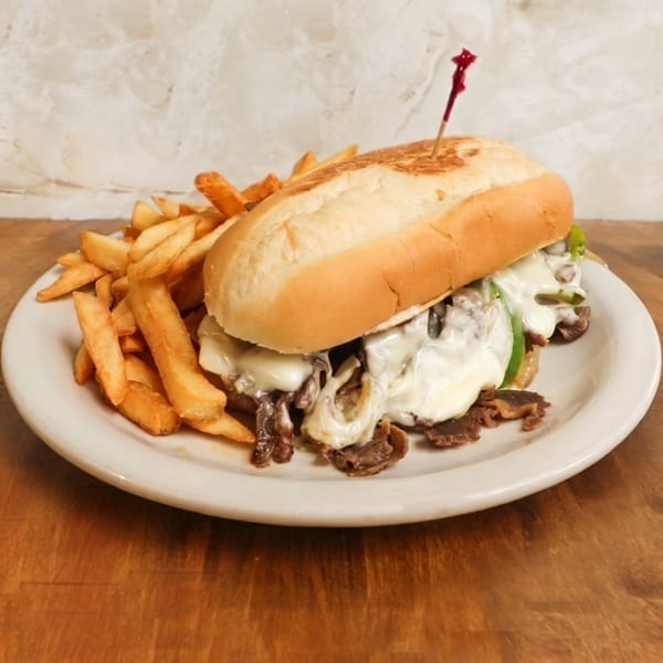 Toasted mushroom-and-cheese sandwich with fries on a white plate atop a wooden table.