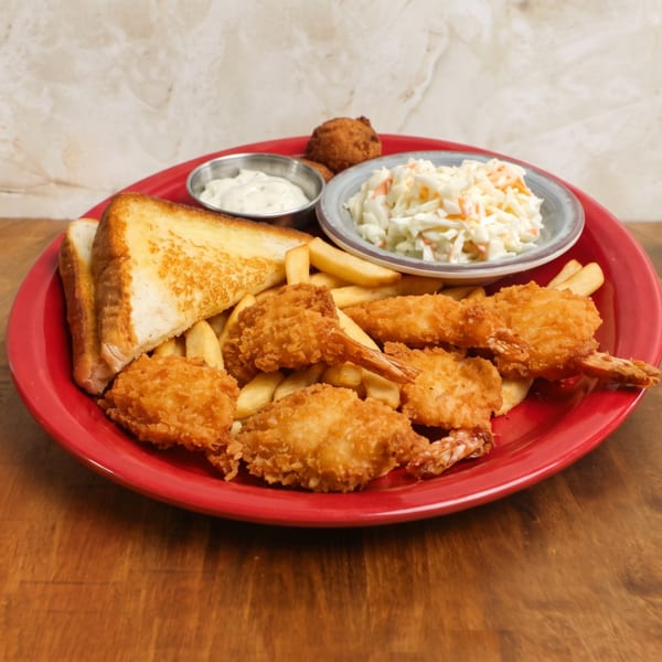 Red platter of breaded shrimp, fries, toast, coleslaw, dipping sauce, and a hushpuppy on a wooden table.
