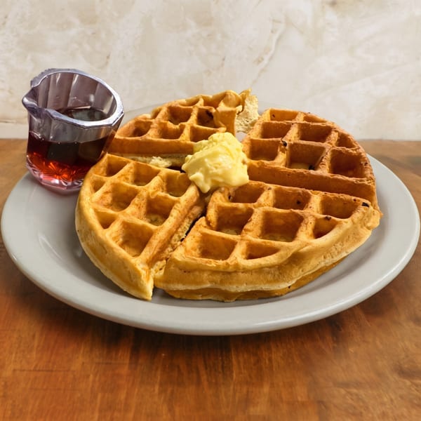 Golden waffles topped with butter and served with syrup on a white plate over a wooden table.